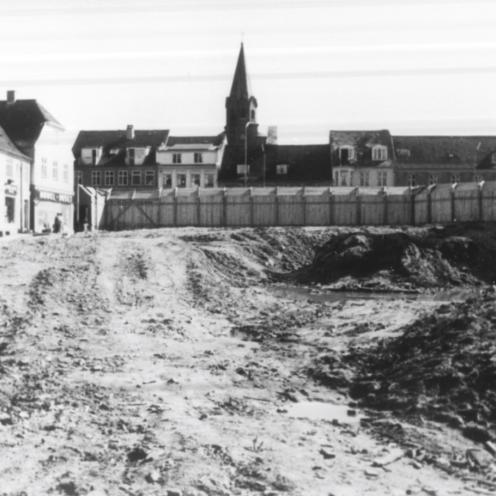 Sort-hvid foto af en tom byggeplads omkranset af bygninger.
