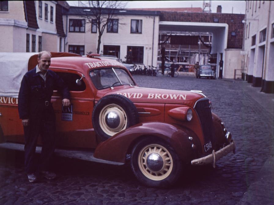 Farvefoto af en medarbejder ved rød servicevogn i baggård.