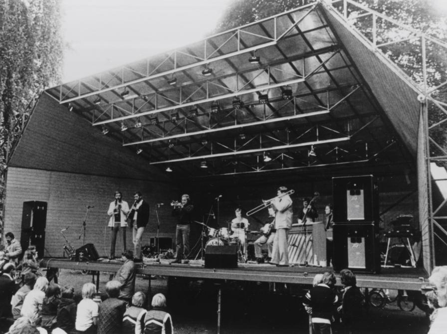 Sort-hvid foto af et orkester, der spiller på en friluftscene foran siddende publikum.