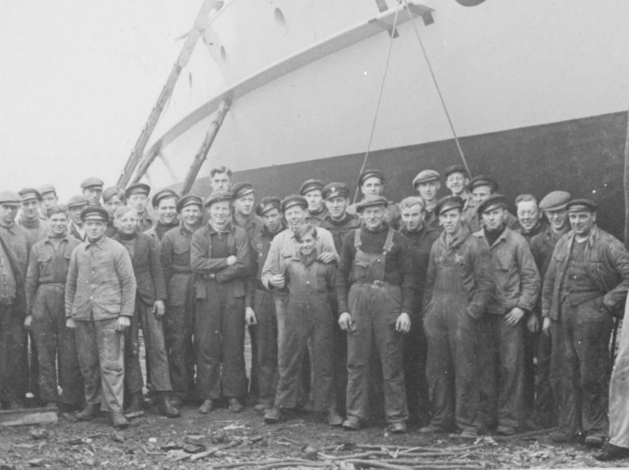 Sort-hvid foto af en gruppe arbejdere foran et skib.