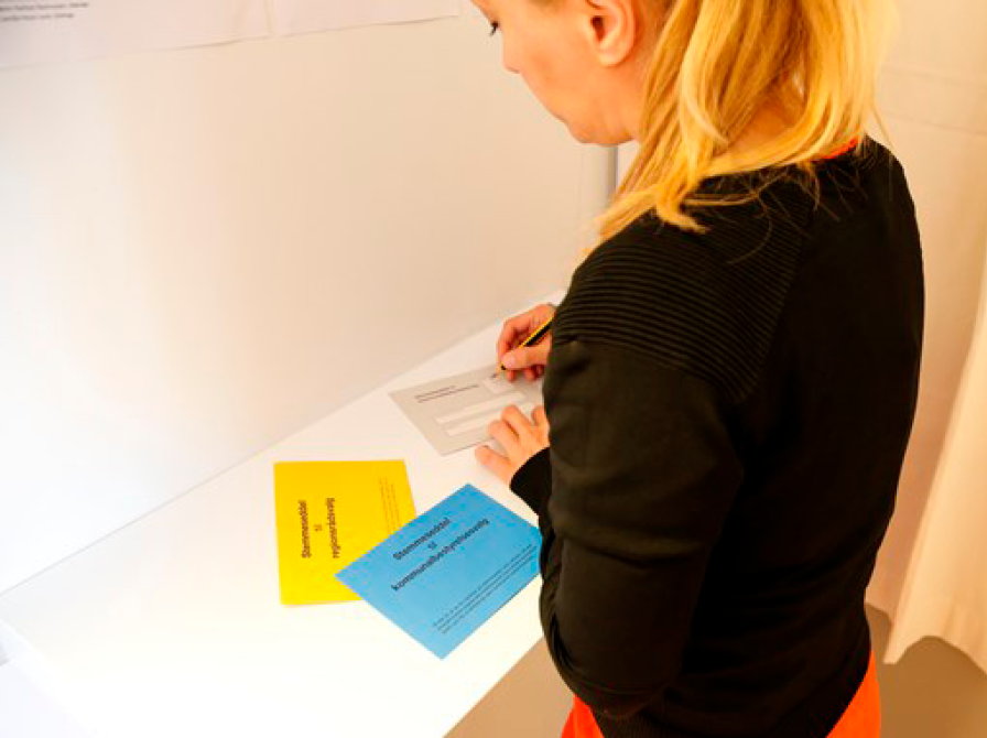 Kvinde med ryggen til, med stemmekortene i en stemmeboks.