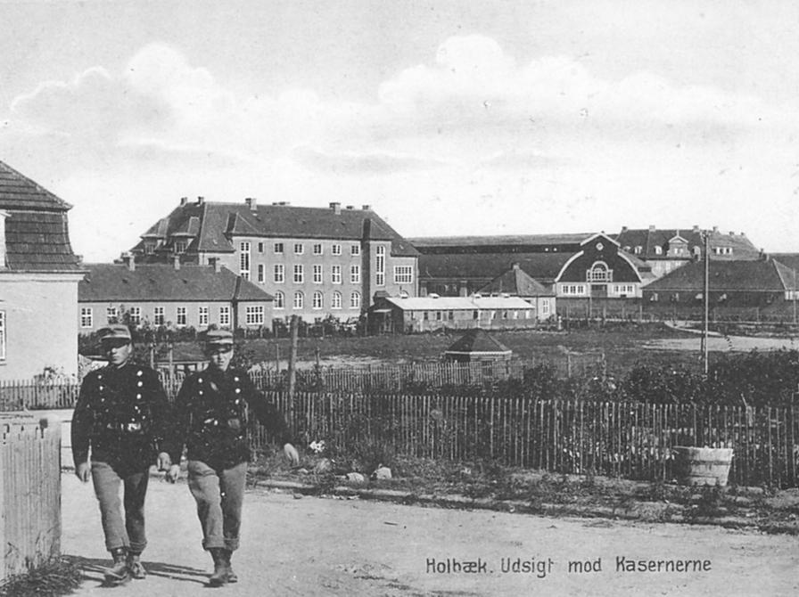 Sort-hvid foto af Holbæk Kaserne og to soldater, der går ad en grusvej i forgrunden.